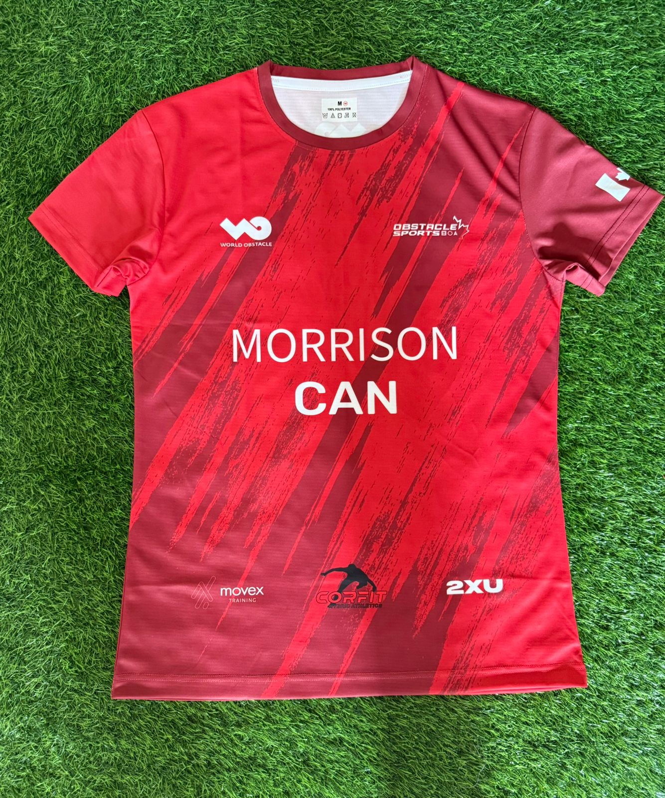 Red sports jersey with 'Morrison Can' text on a green grass background